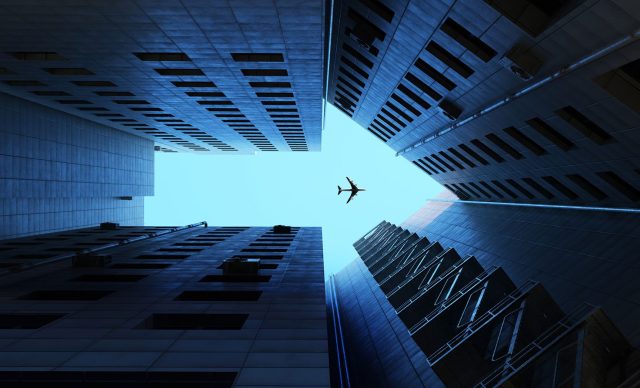 Airplane flying on blue sky, above buildings