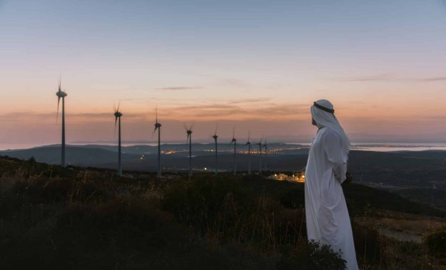 Middle Eastern Businessman in wind turbine farm at sunset