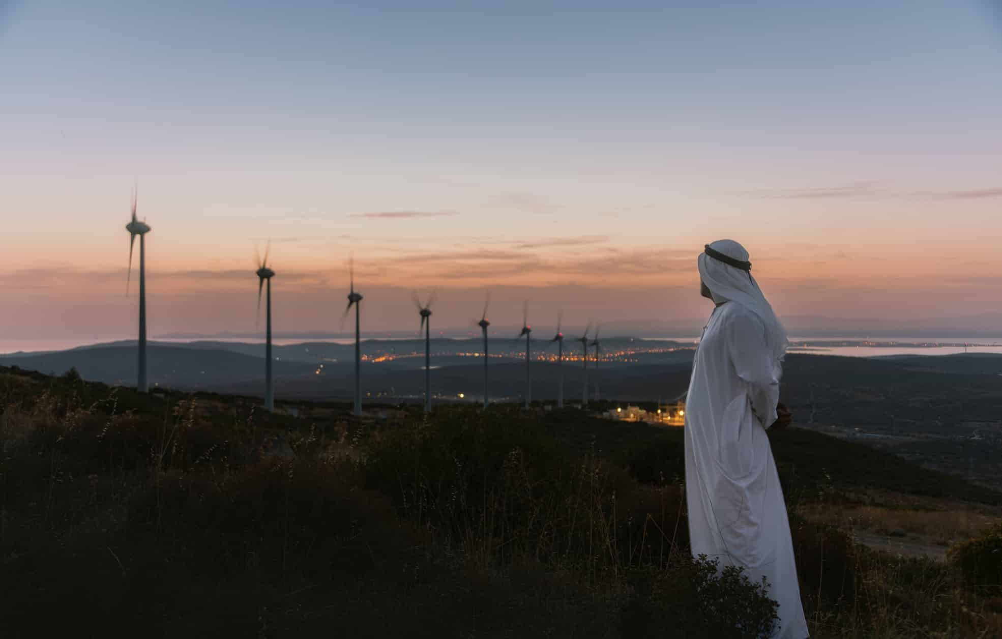 Middle Eastern Businessman in wind turbine farm at sunset