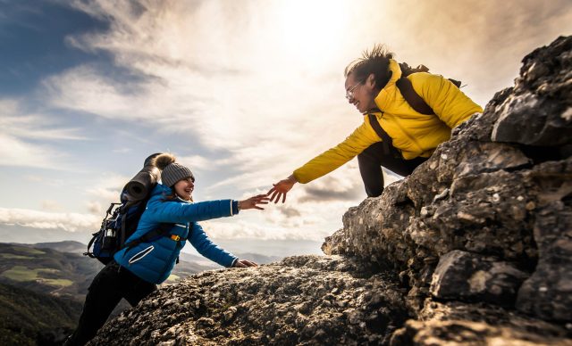 People helping each other hike up a mountain