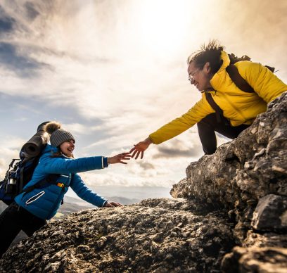 People helping each other hike up a mountain