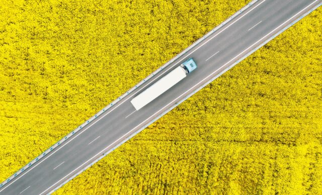 Overhead view of a semi truck driving between canola fields