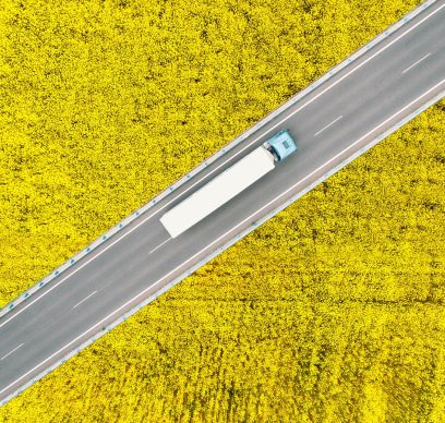 Overhead view of a semi truck driving between canola fields