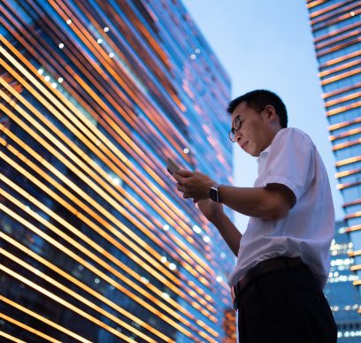 A young Asian businessman wearing a white shirt is using a smartphone